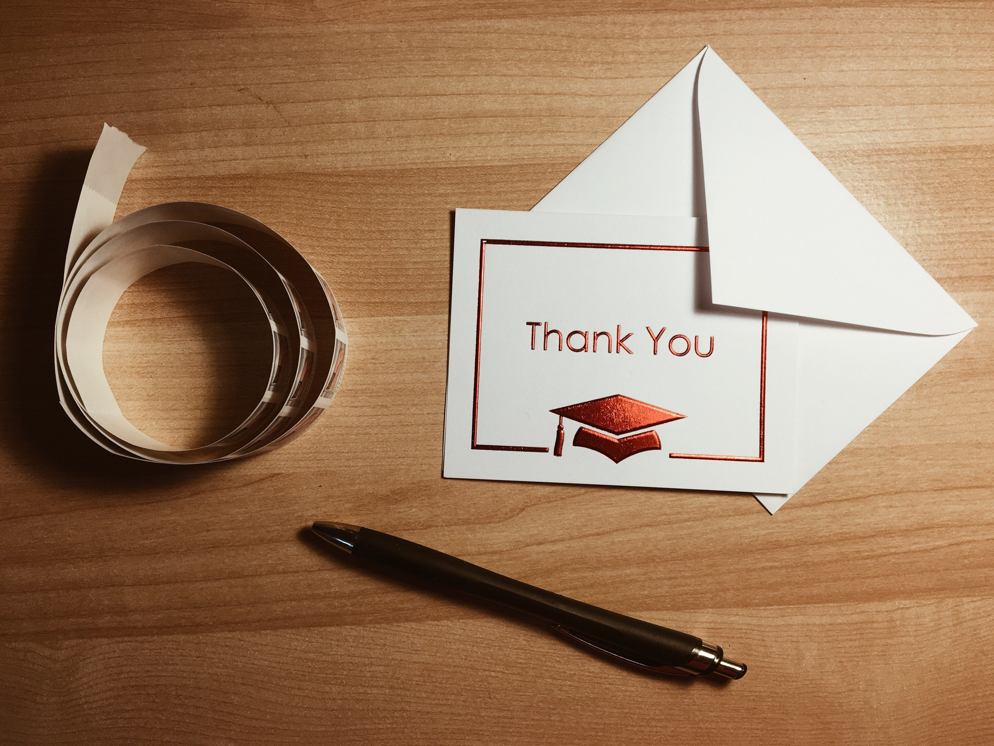 A thank you card with a graduation cap on the front with a roll of stamps and pen