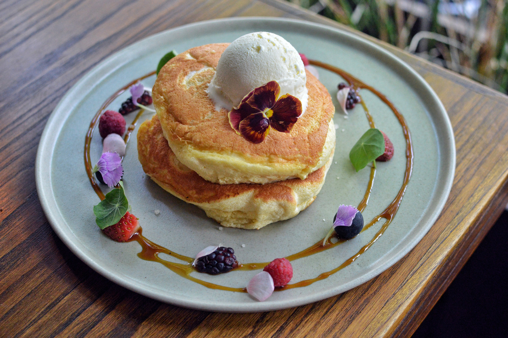 a plate of pancakes topped with butter and a flower and with syrup and fruit decorated around