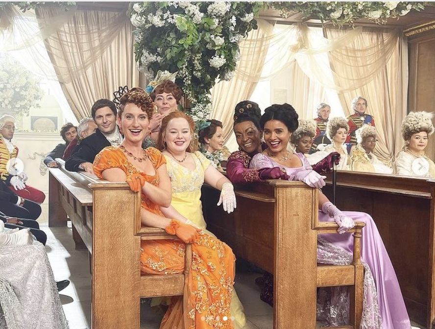 the group of actors turn to smile at the camera while sitting in the church pews