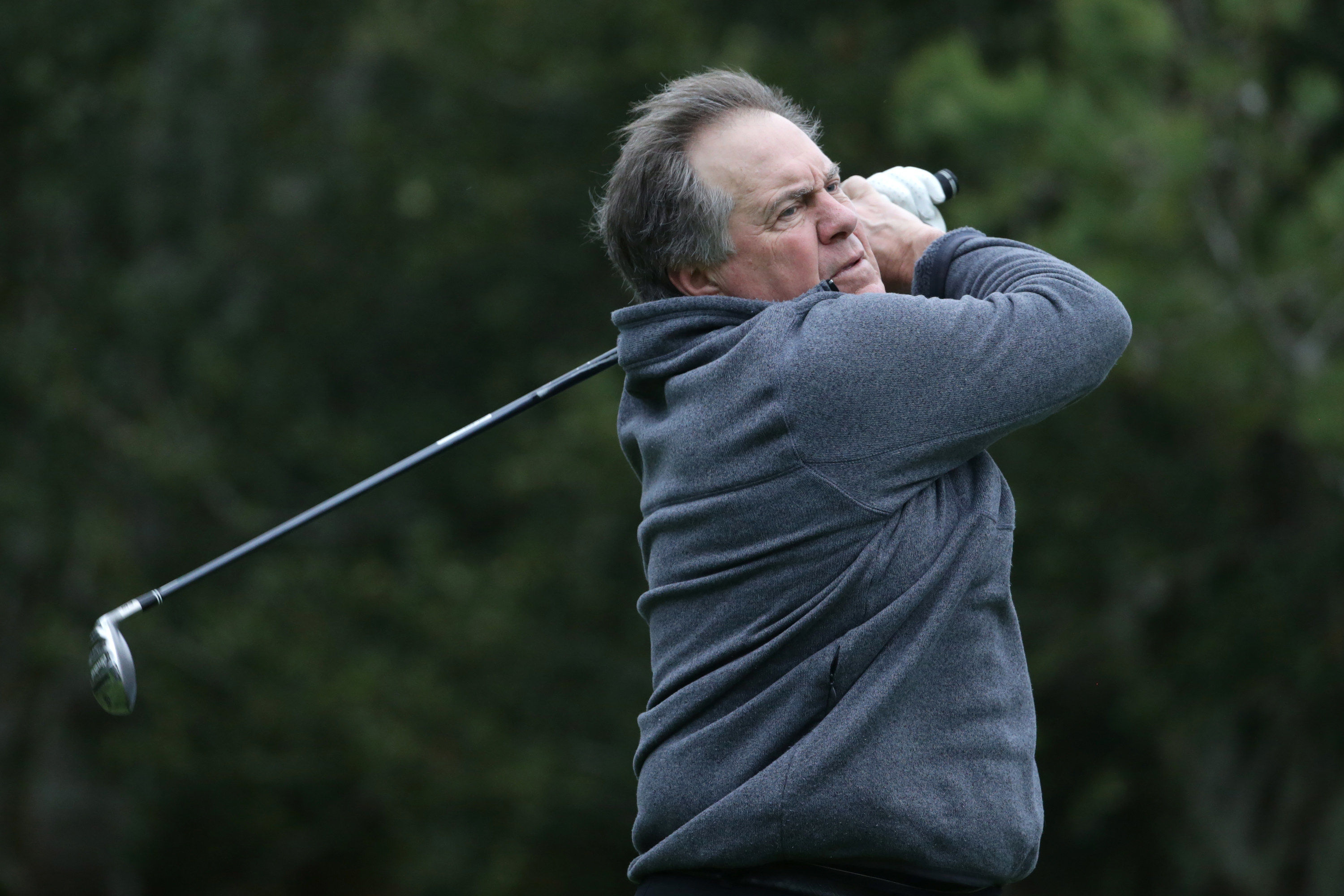 Bill Belichick swings a golf club