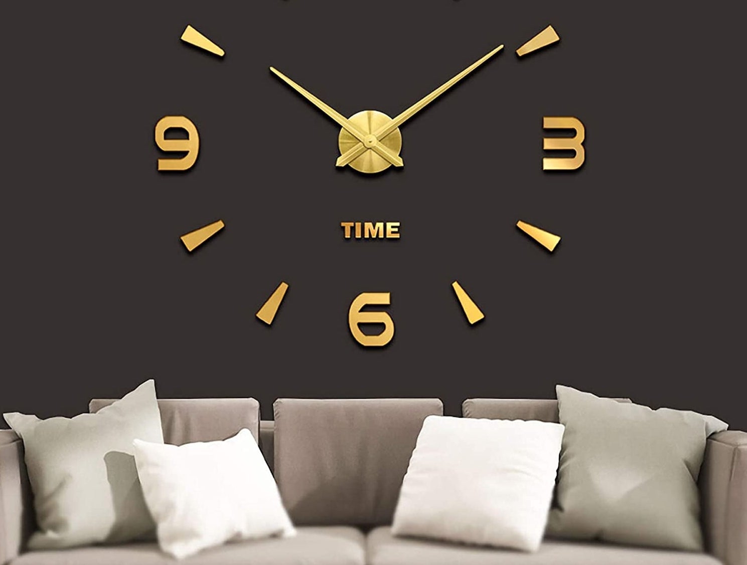 The clock mounted above a couch with four cushions on it