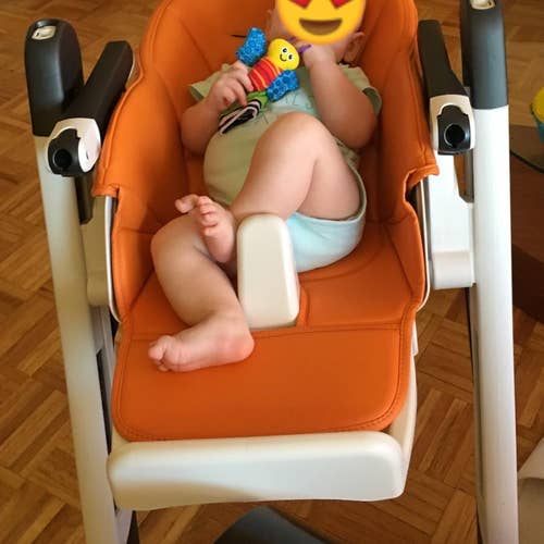 reviewer's photo of the orange high chair in recline position with a baby inside