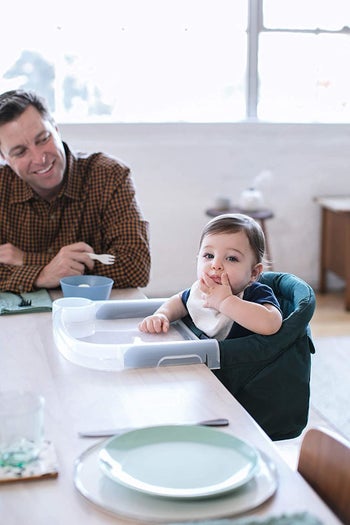 A model smiles at a baby who is sitting in the high chair attached to a table