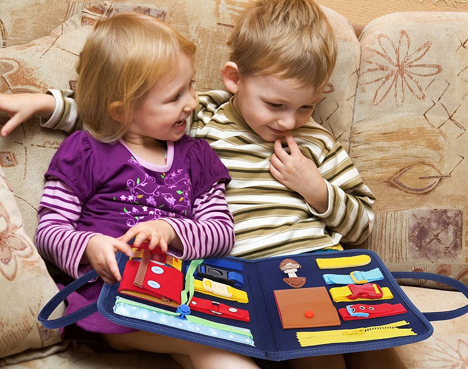 Two kids on a couch playing with the busy board