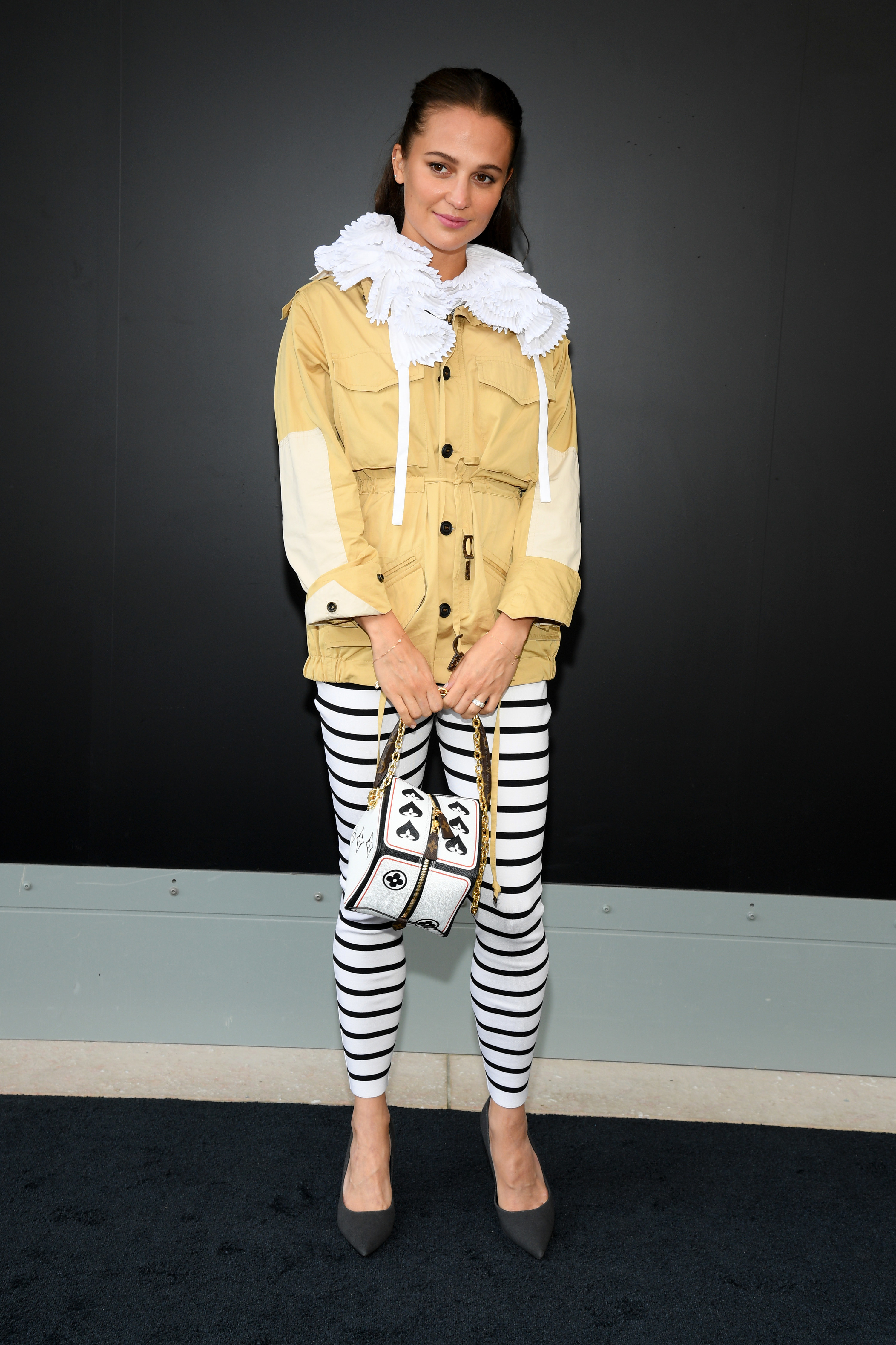 Alicia Vikander in horizontal-striped leggings and holding a small bag on the red carpet