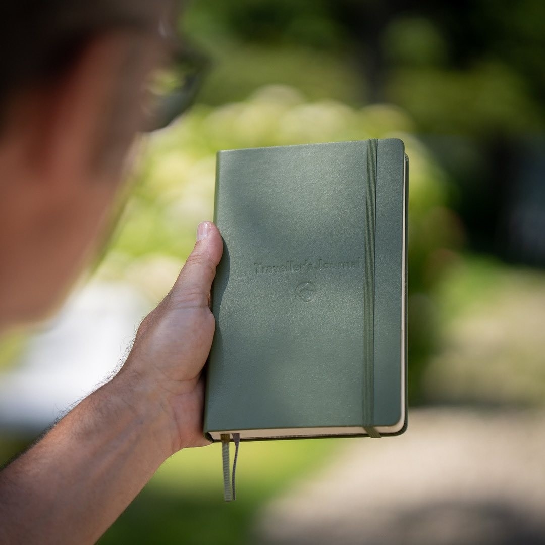 A person holding the journal in front of a blurred grassy background