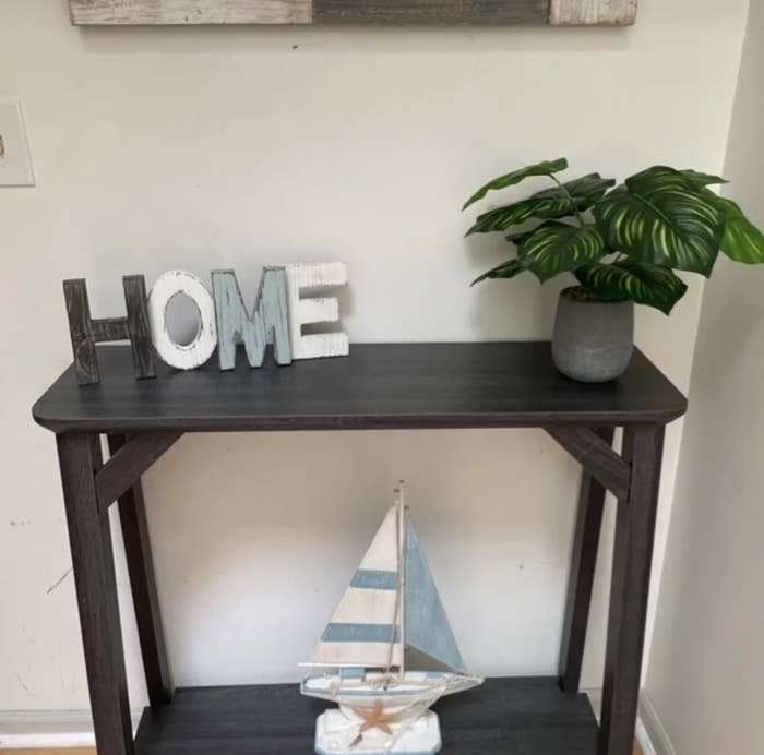 reviewer&#x27;s photo of the brown white and blue HOME sign sitting on hall entryway table