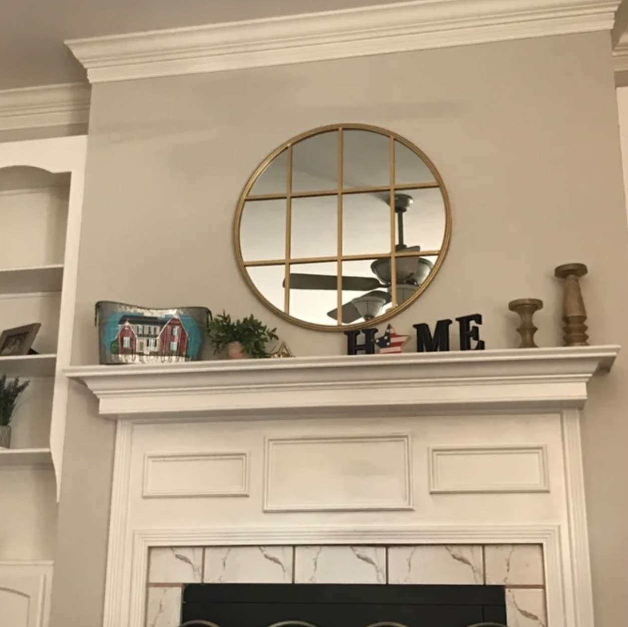 reviewer&#x27;s photo of gold circular mirror hanging about mantlepiece