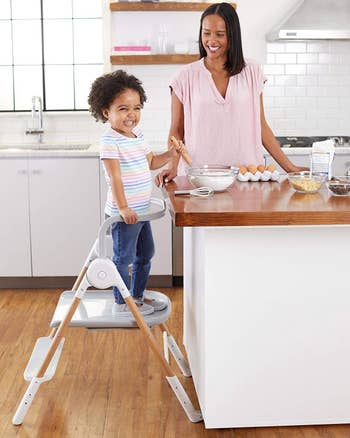 A toddler standing in the kitchen helper and baking with their parent