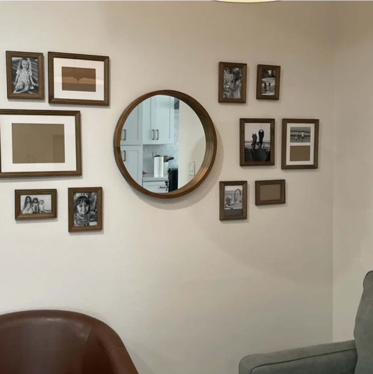 reviewer&#x27;s photo of the brown wood frames spread about the wall surrounding a round accent mirror, some with photos and some still empty