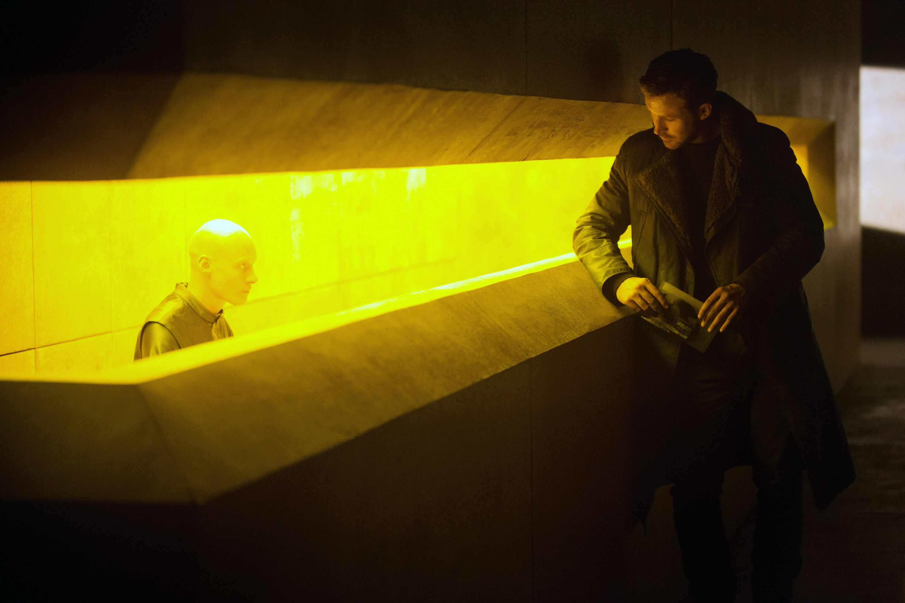 Ryan Gosling at a futuristic office front desk bathed in yellow light