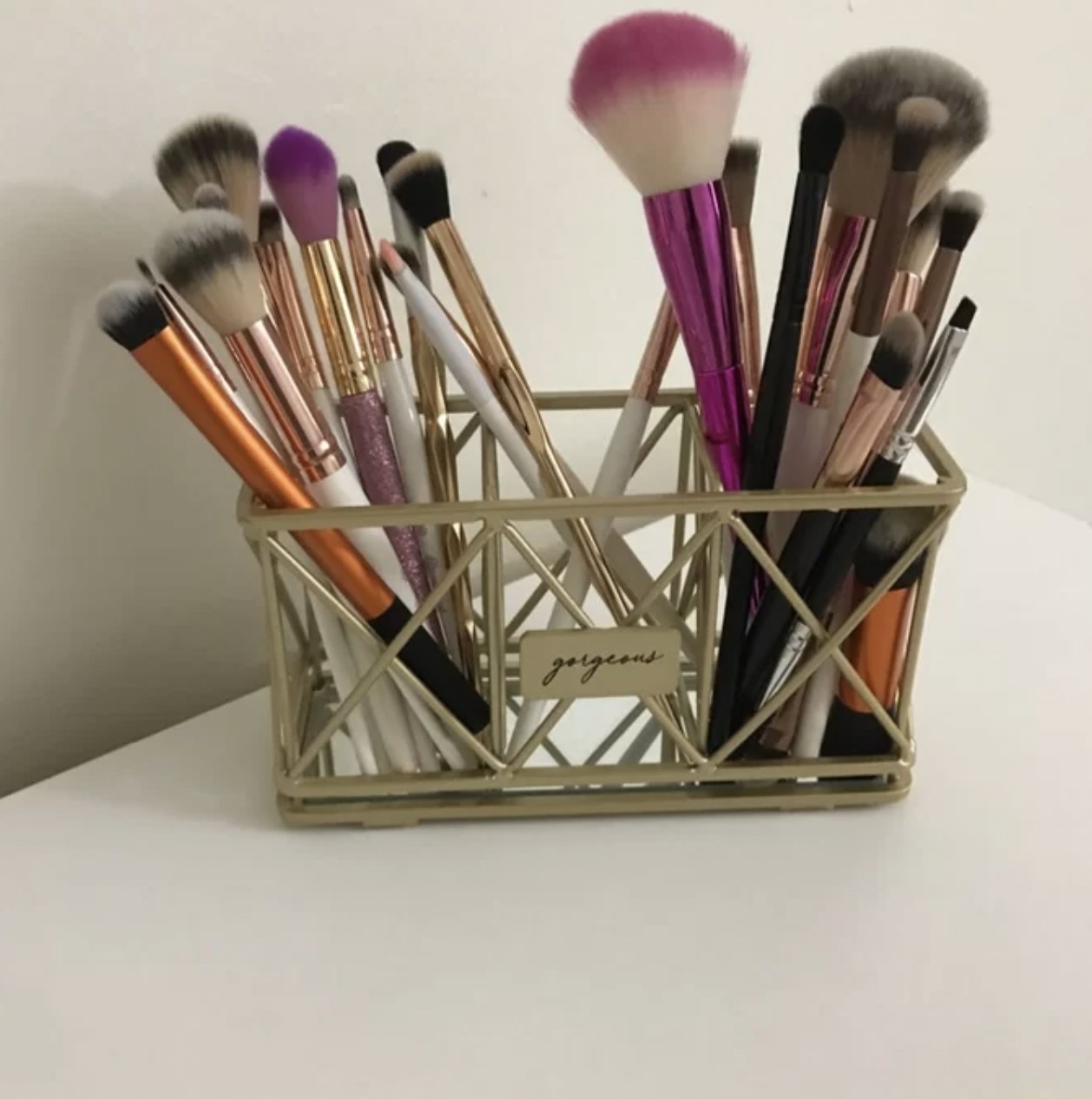 Reviewer&#x27;s photo of the gold-finished geometric organizer holding their makeup brushes