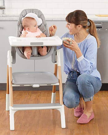 A model feeding a baby who is sitting in the gray high chair
