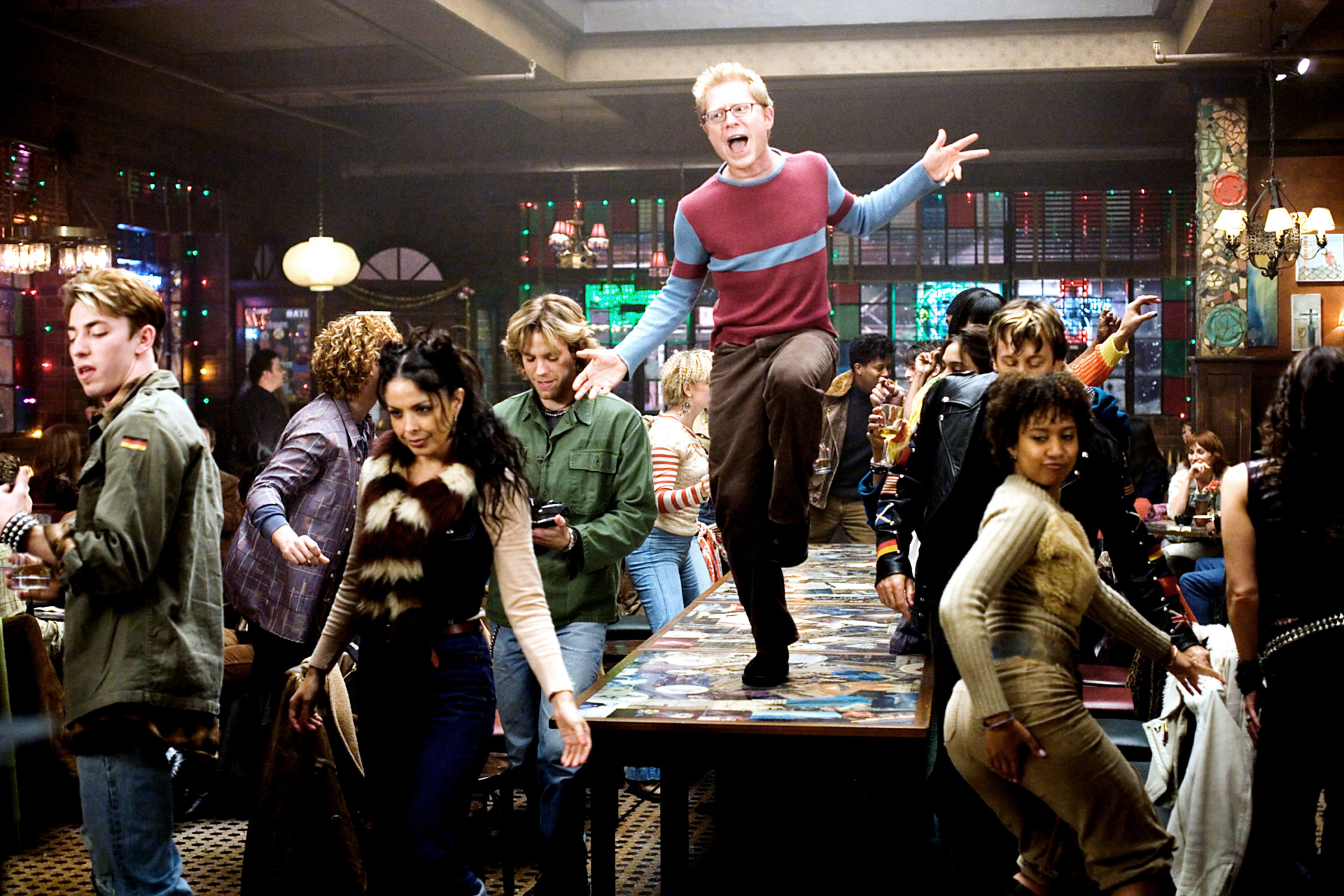 Anthony Rapp dancing on a table surrounded by the cast
