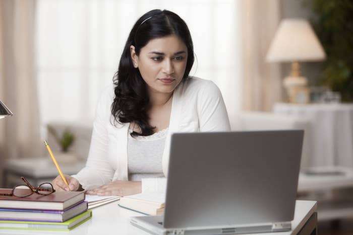 person writing in a notebook and looking at a laptop screen