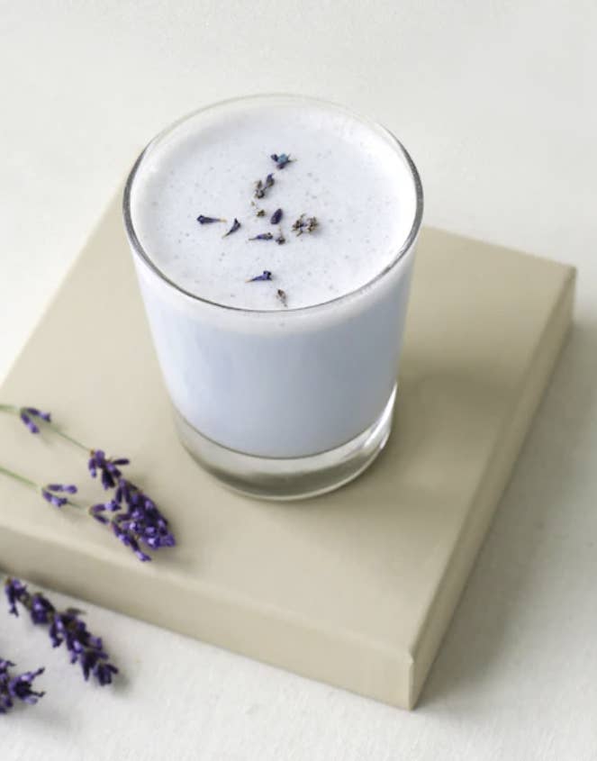 A glass of the Blume drink on a square platform, with some sprigs of lavender next to it