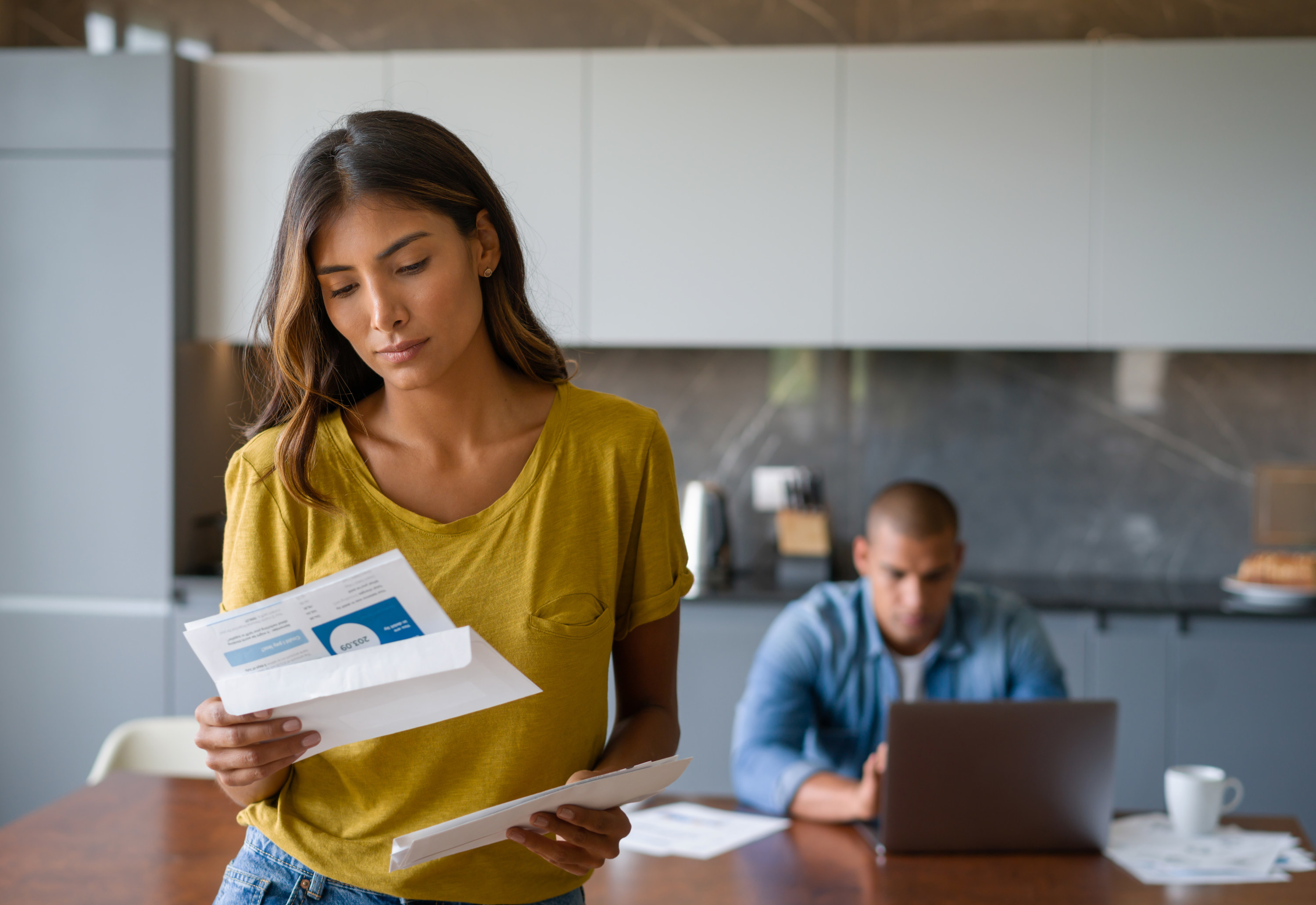 A woman in the kitchen with a man looking at bills