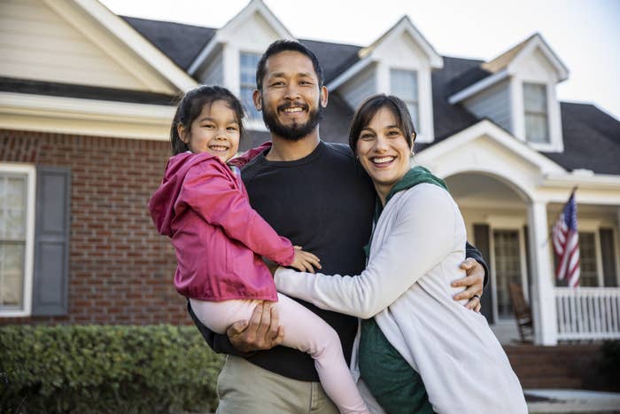 family of three standing in front of a house