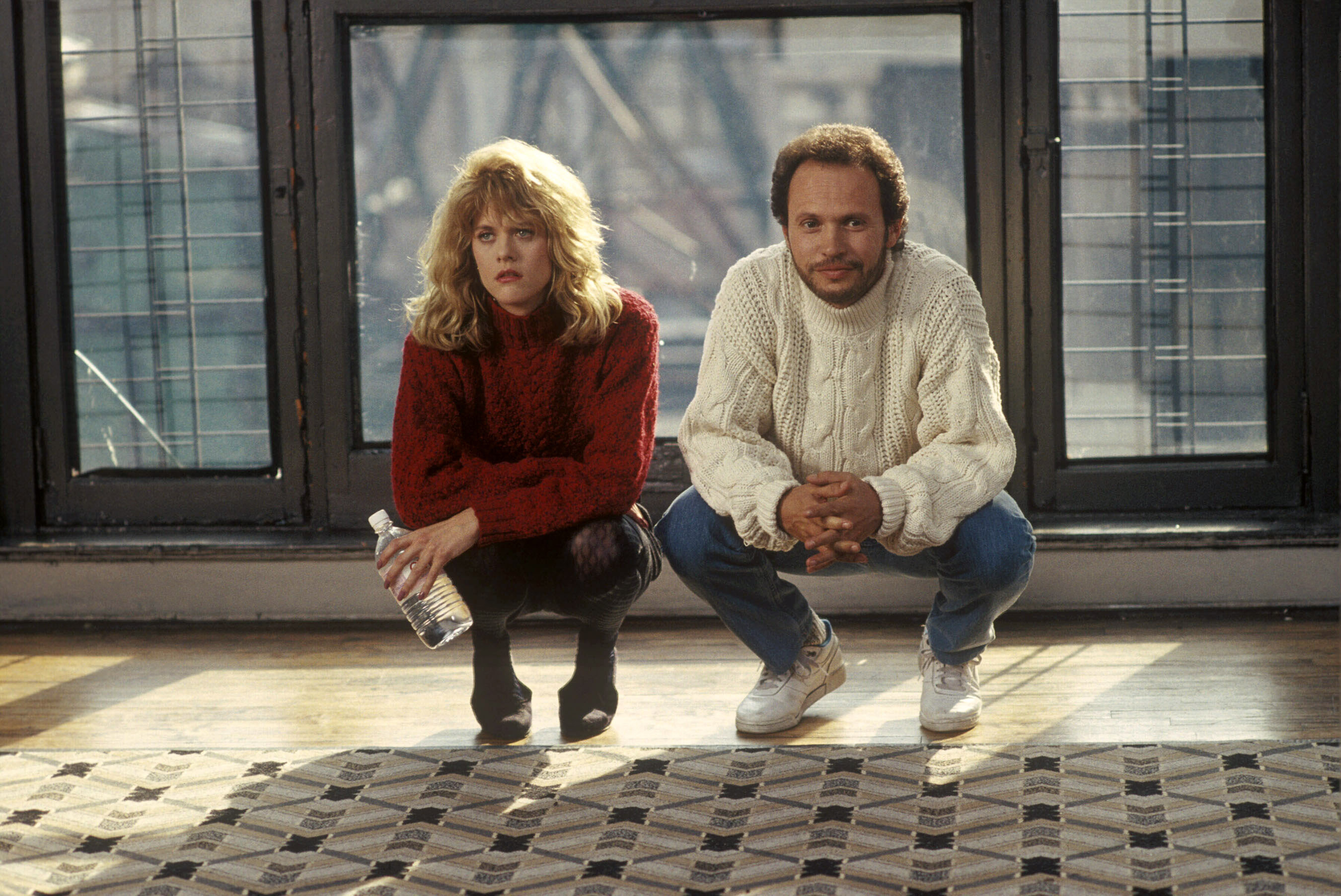 Meg Ryan and Billy Crystal squatting next to a large rug