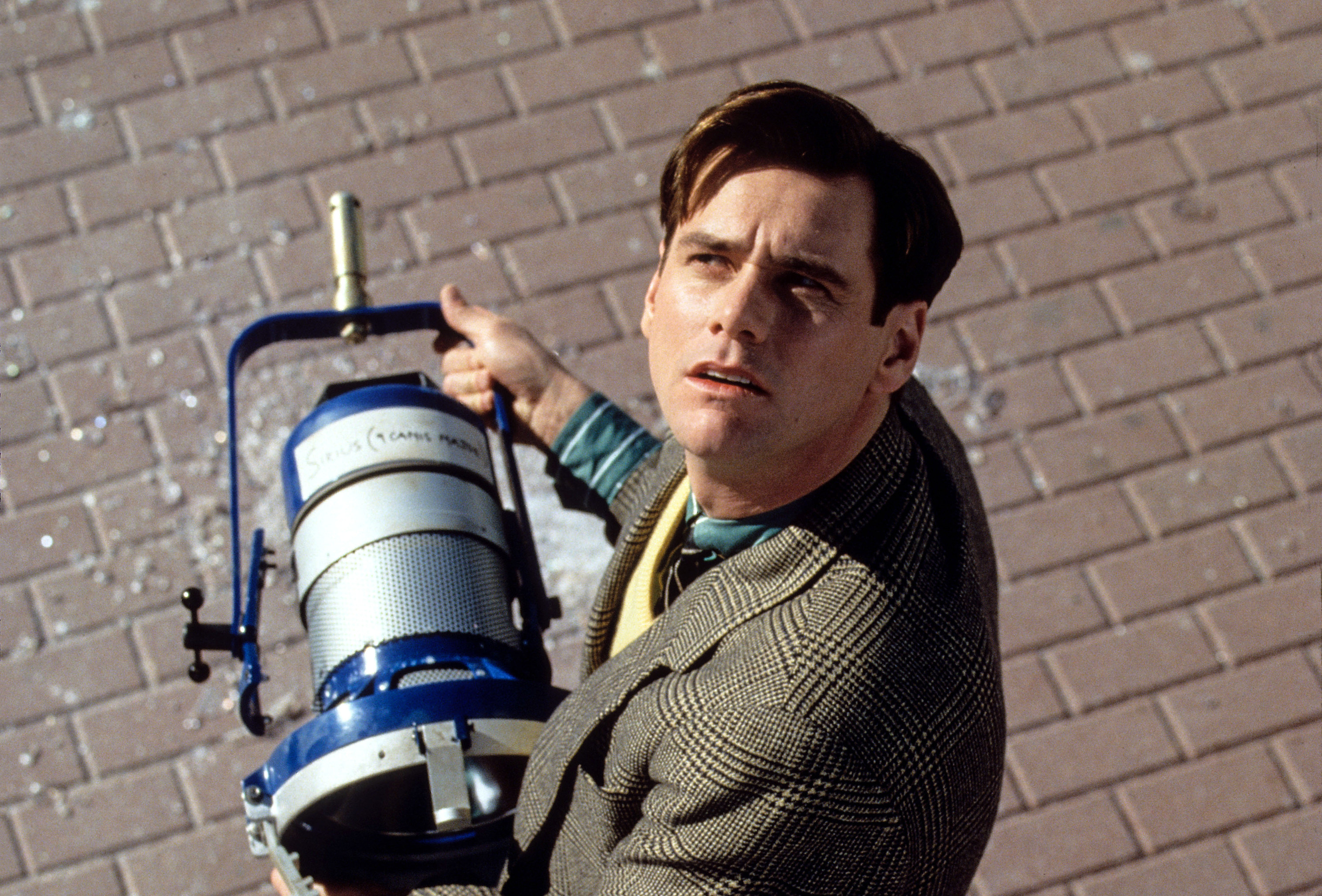 Jim Carrey holding a television set light and looking up suspiciously