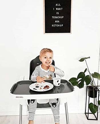A child eating their food from the large tray attached to the high chair