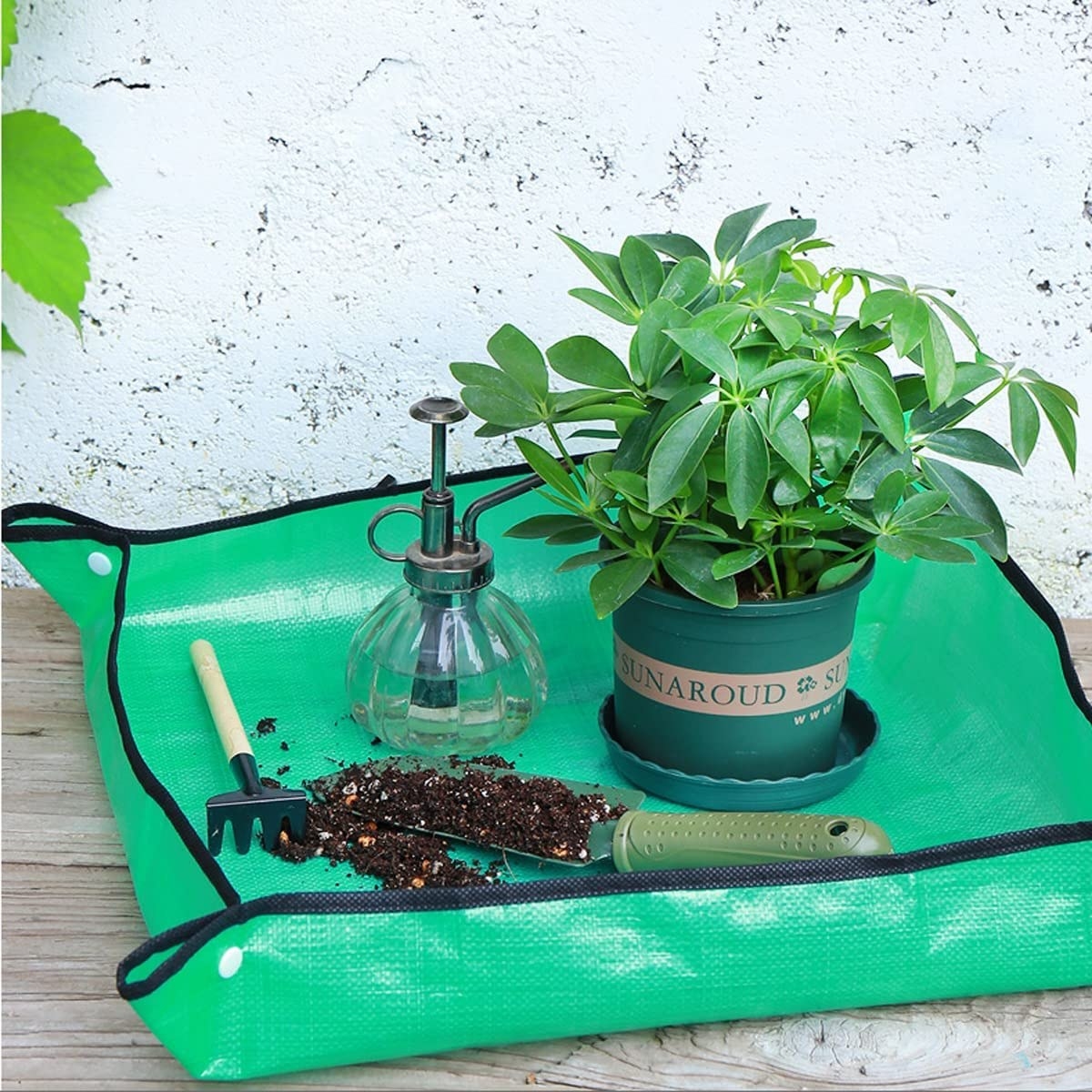 A square mat with a plant, small shovel and mister on it