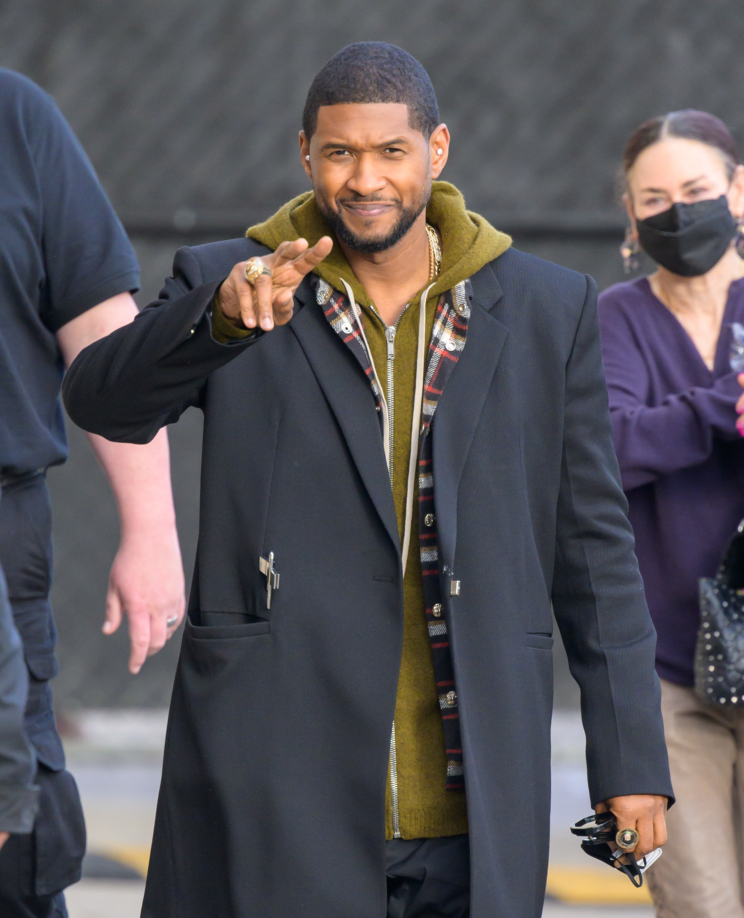 Usher smiling and giving the peace sign with people around him outside