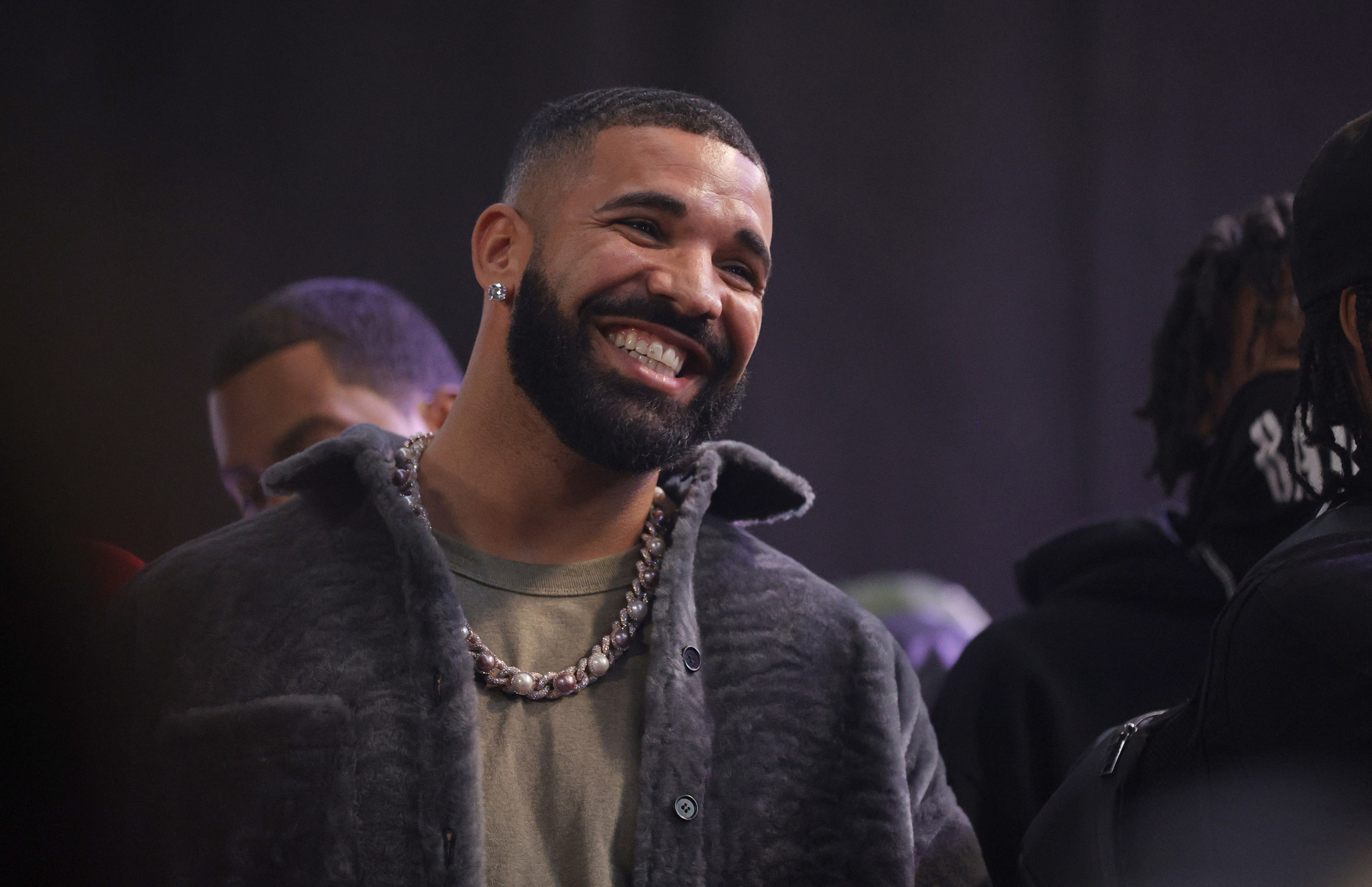 Drake smiling with people behind him