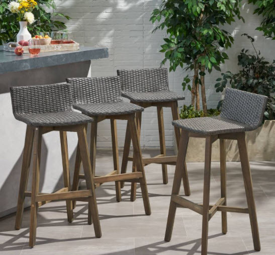 A set of 4 bar stools with wicker material seats and wooden legs. Each includes a leveled footrest and small backrest.