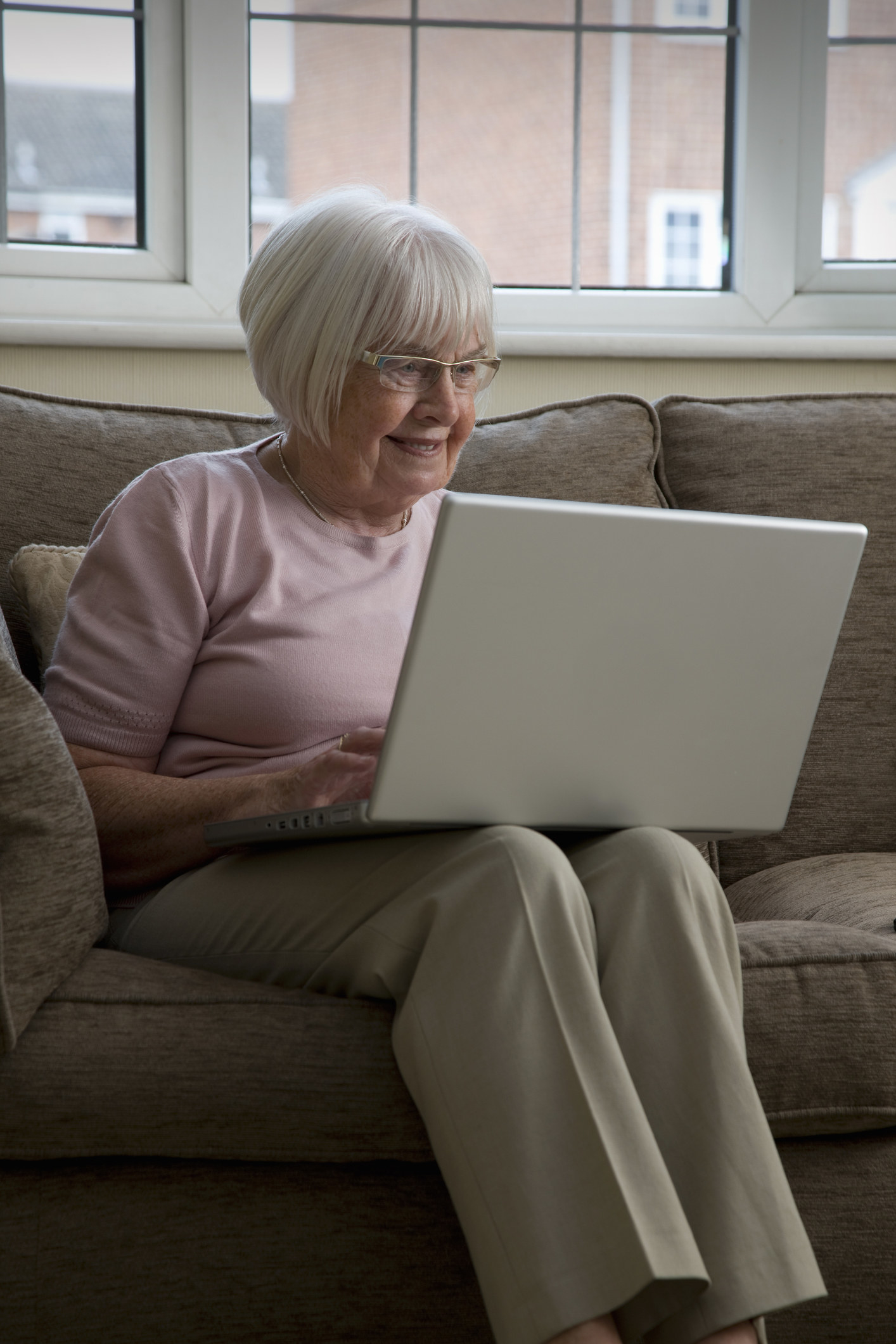 An elderly woman smiling while using her laptop.