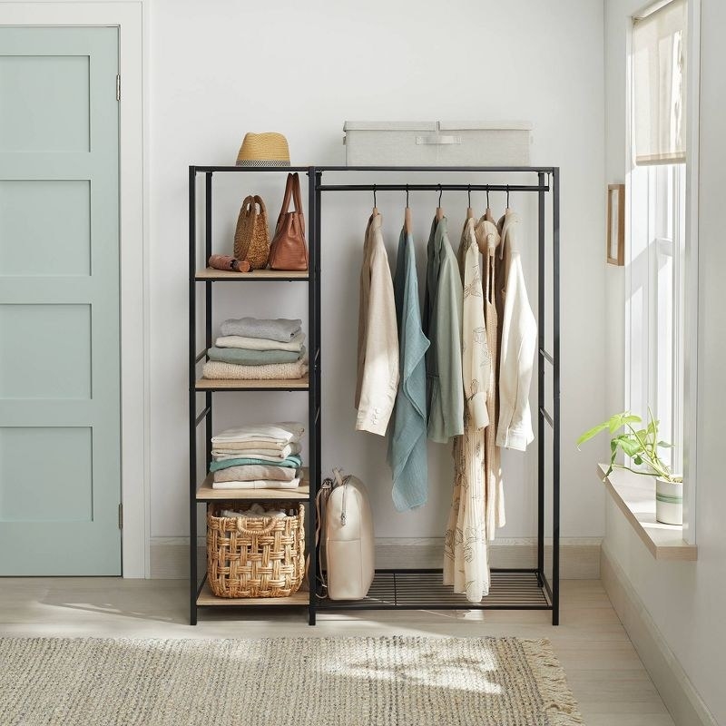 A tidy metal rack with shelves holding folded clothes, bags, and a wicker basket; jackets hang from the rod