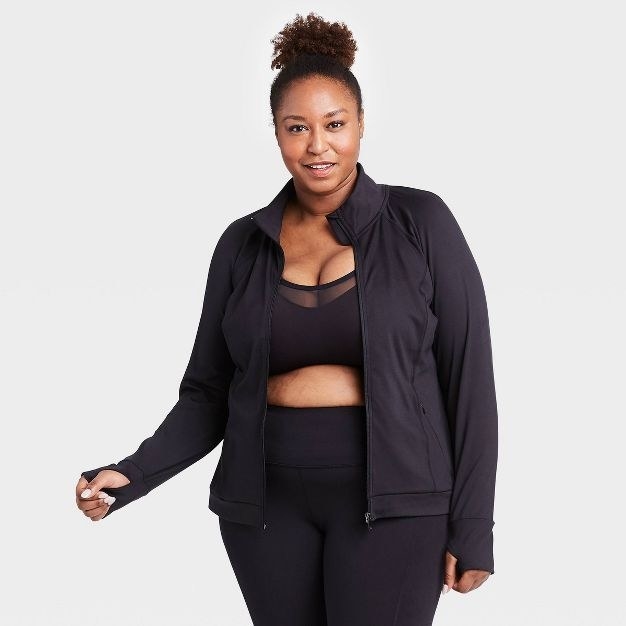 a model wearing the jacket in black with matching leggings and sports bra