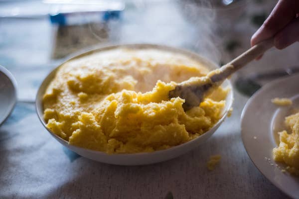 Close-up of a wooden spoon serving polenta from a plate on a dining table