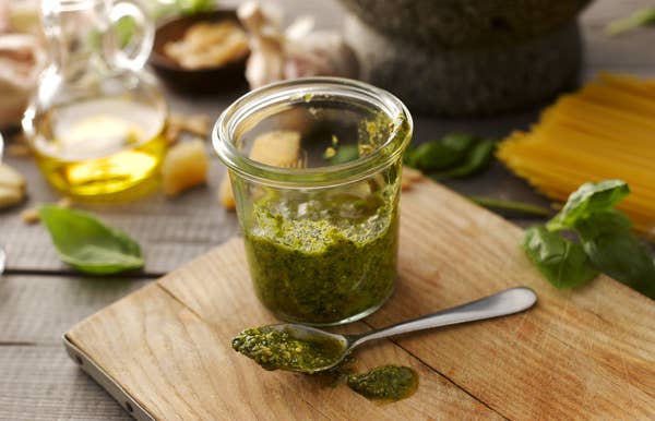 A jar of pesto and a spoon on a cutting board