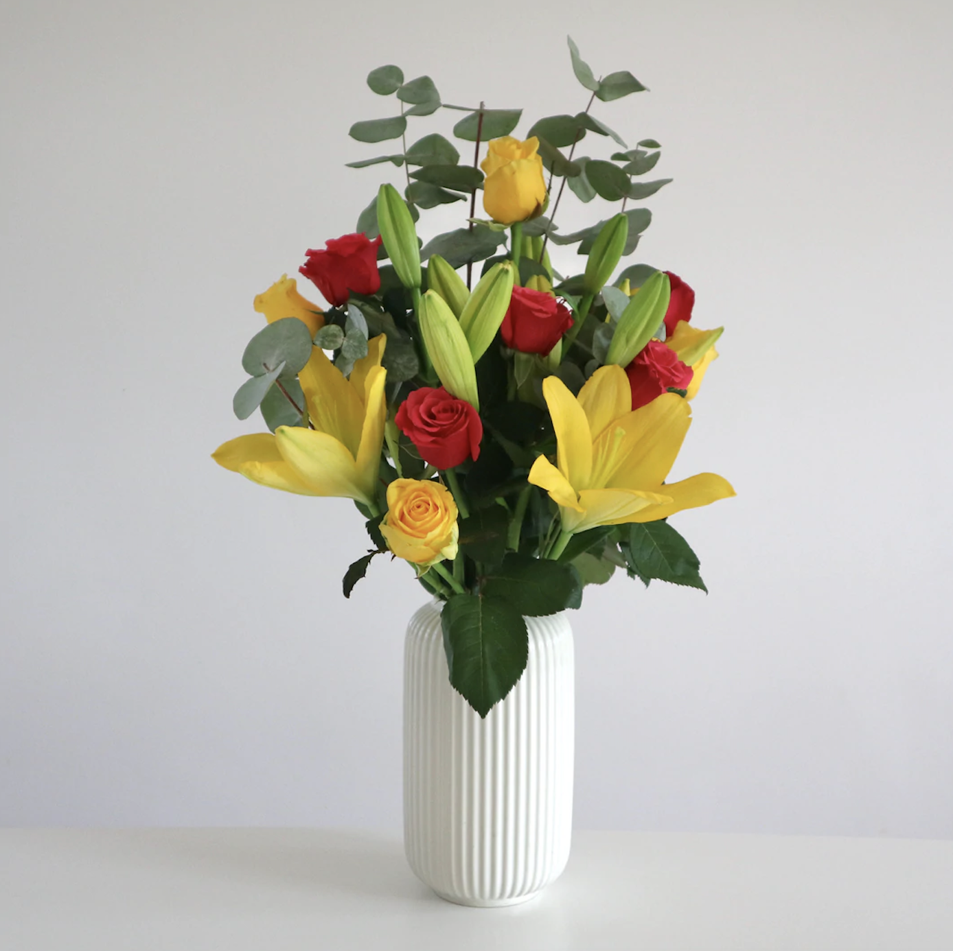 A beautiful arrangement of yellow lilies, red and yellow roses and mixed foliage