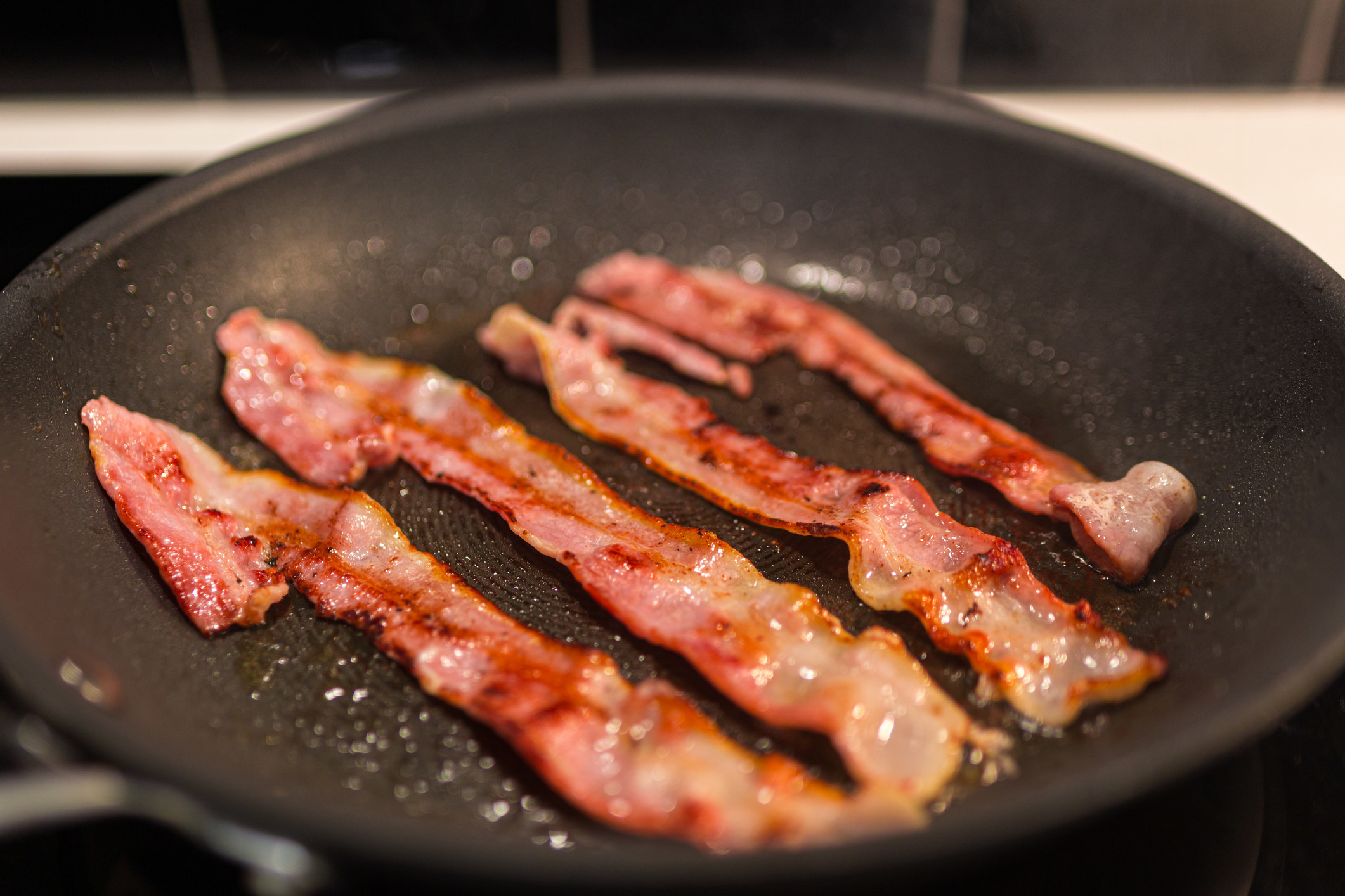 four strips of bacon frying in a pan