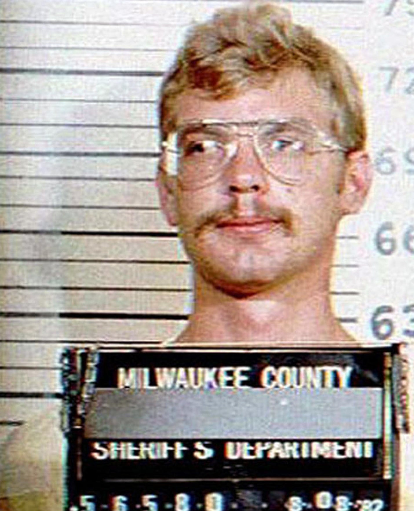 Jeffrey Dahmer's mug shot wearing silver rimmed glasses and a mustache
