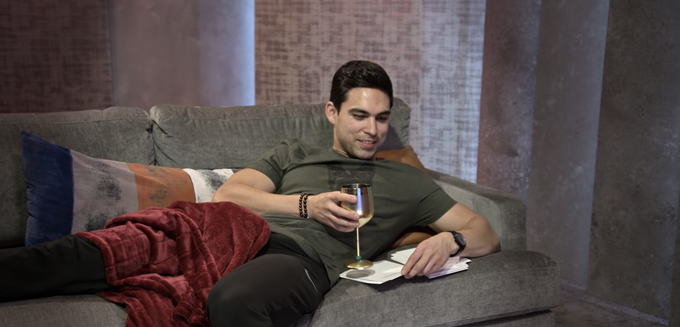 one of the men gets comfy on the couch with a glass of wine and his notes