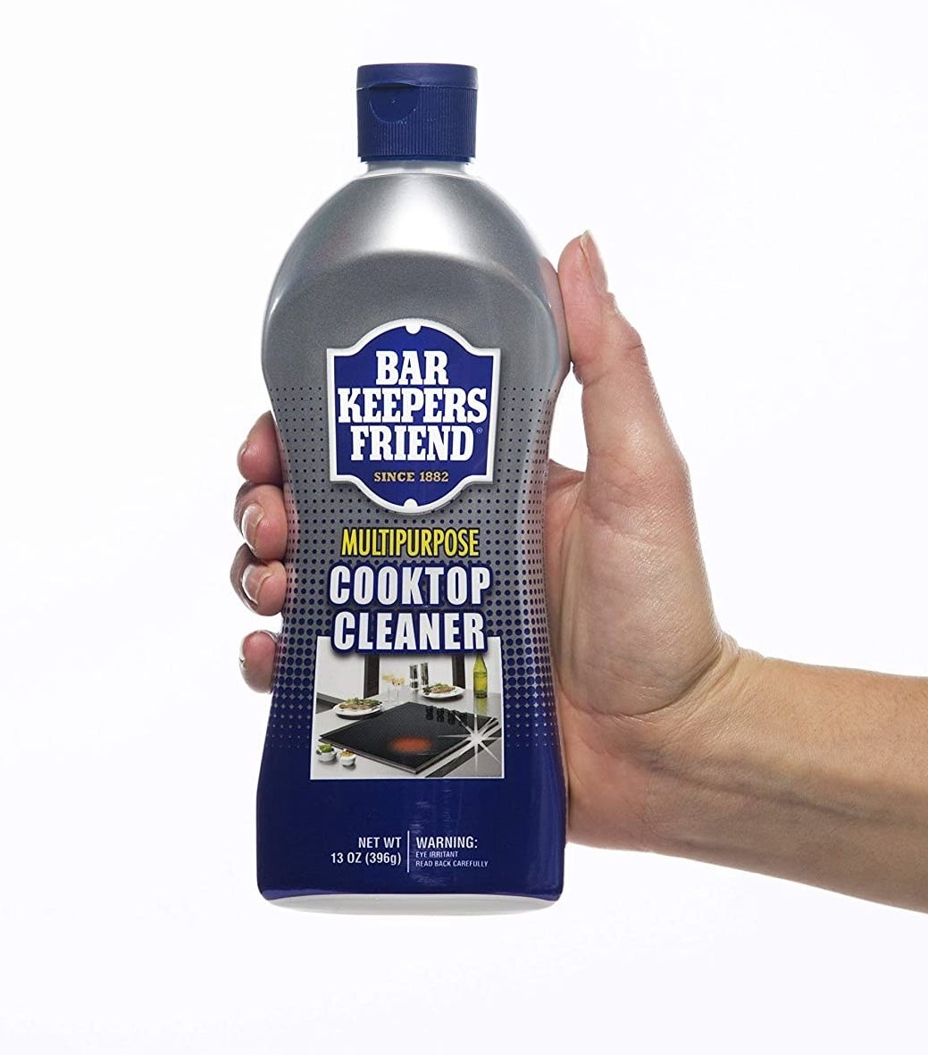 A person holding a bottle of cooktop cleaner