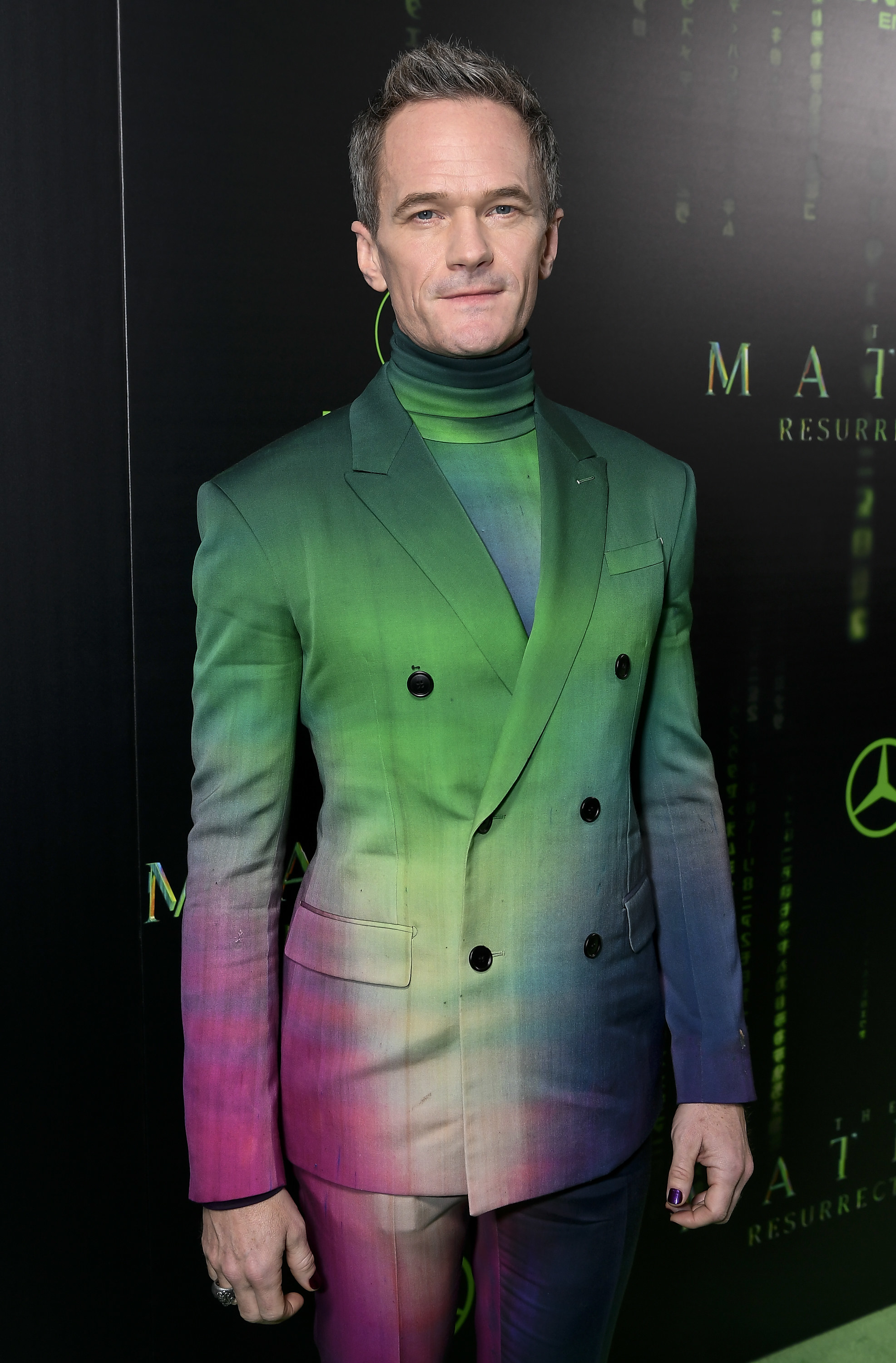 Neil wears a suit that is traditional in fit, but is a gradient from green to purple, with a matching green gradient high-neck top underneath