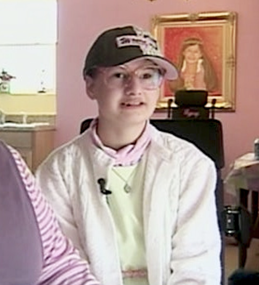 Gypsy sitting for an interview wearing a jacket, hat, and glasses