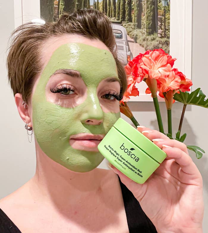Victoria wearing the matcha clay mask on her face while holding up a jar of the mask