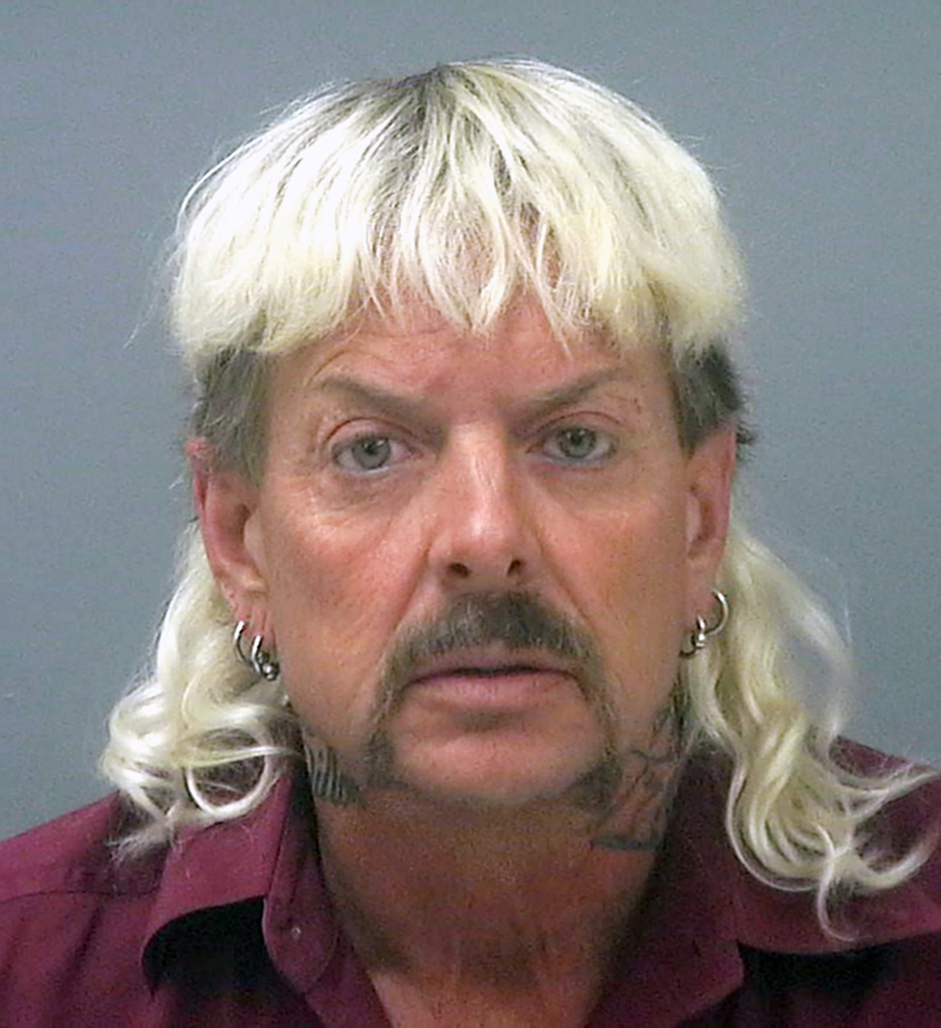 Joe Exotic mug shot where his hair is bleached blonde and in a mullet and multiple piercings
