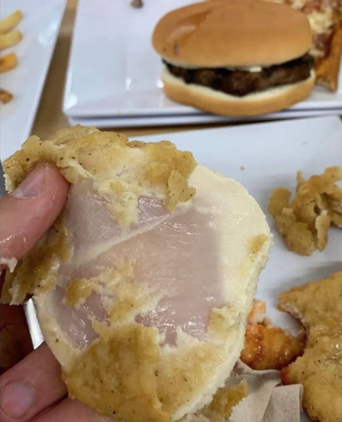 a hand holds up an undercooked piece of chicken