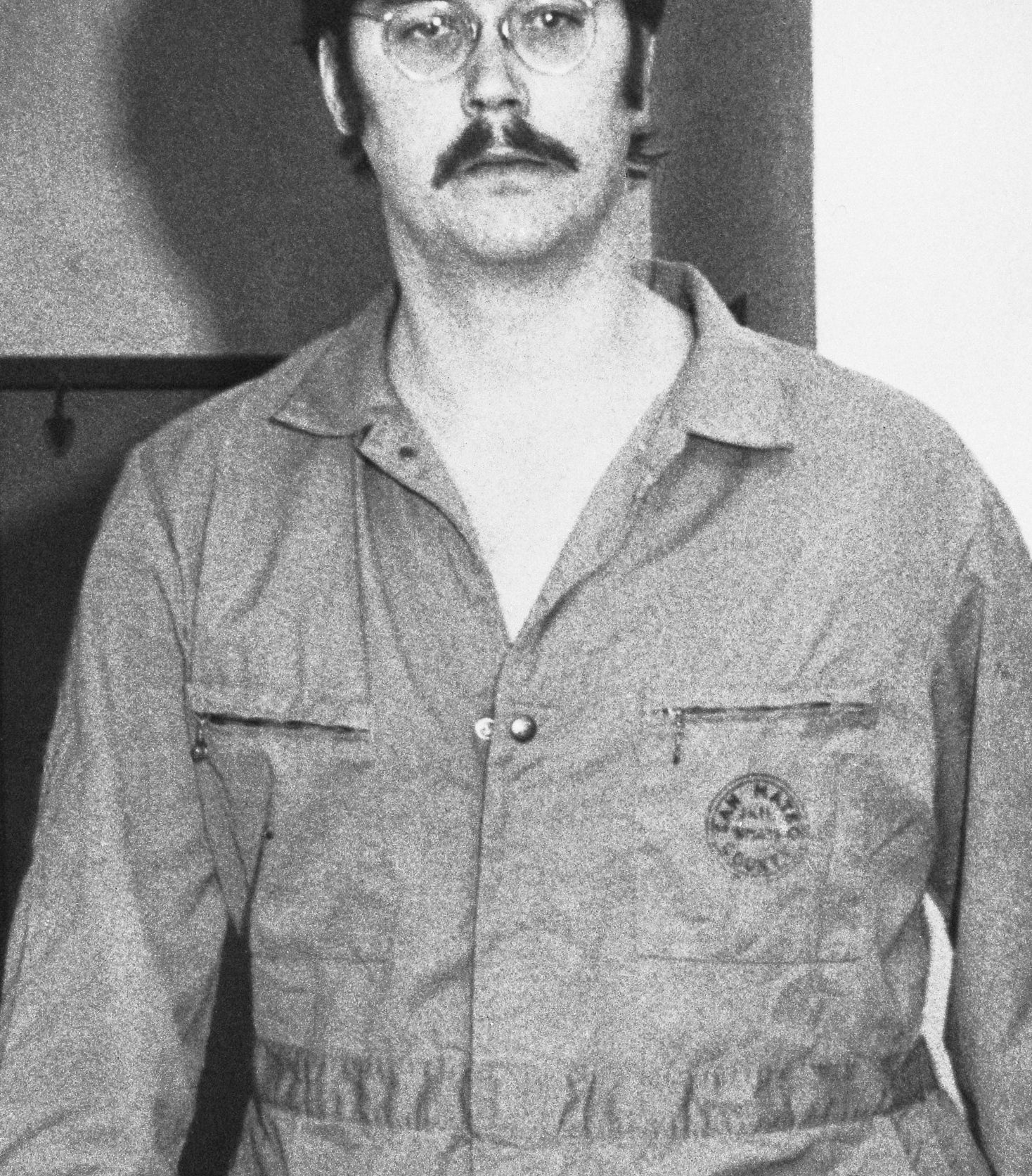 Edmund in his prison uniform with a mustache and glasses
