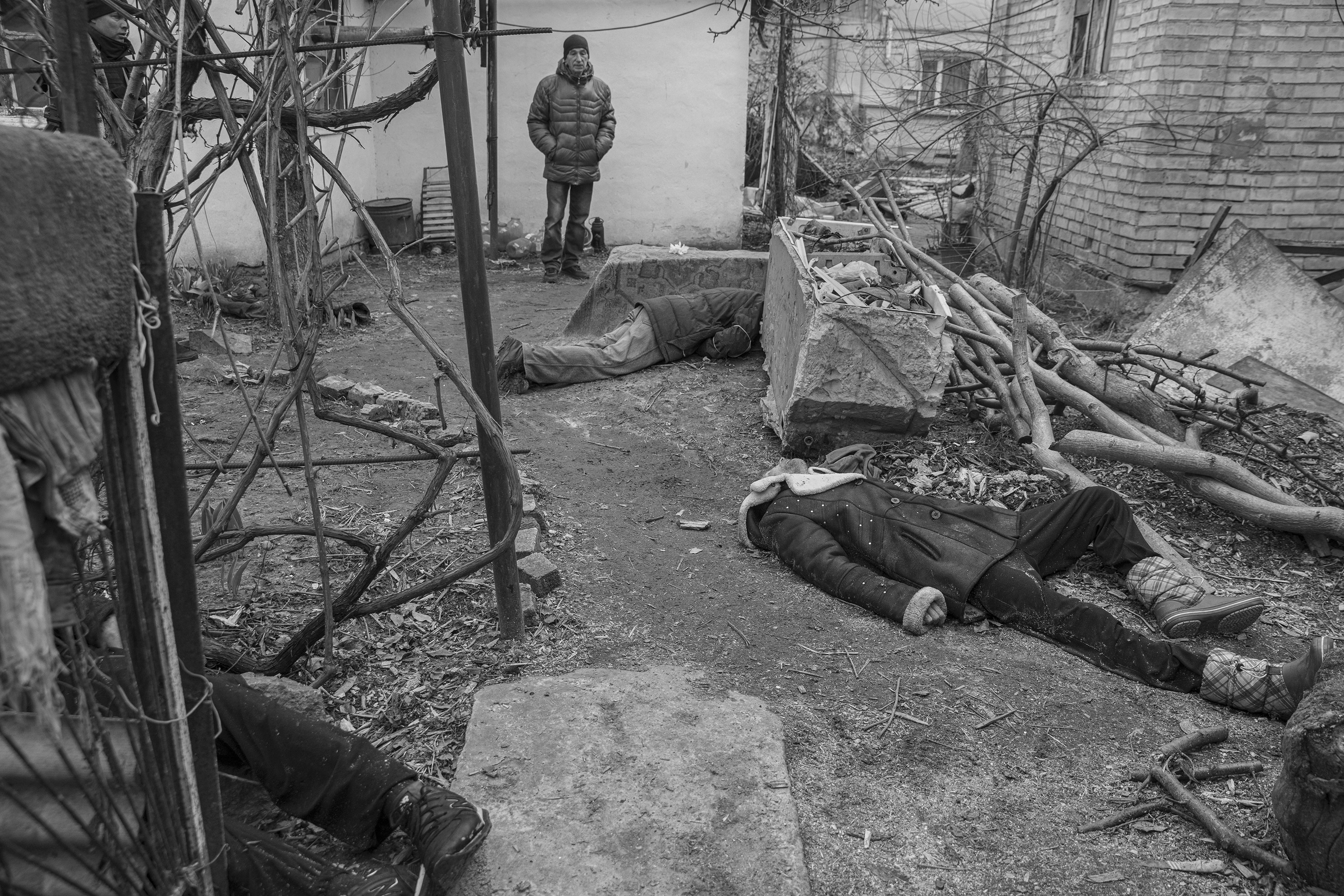 A man stands amid a barren area with several corpses lying on the ground in a black-and-white photo