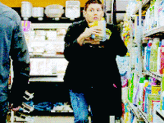 Jensen Ackles as Dean Winchester in a supermarket in &quot;Supernatural&quot;, holding a bunch of products in his arms and slow-jogging away