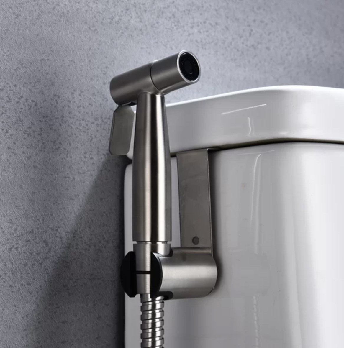 The stainless steel handheld bidet is hooked up to the side of the white toilet