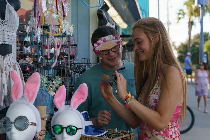 Colton Ryan and Elle Fanning stand at an outdoor display of accessories like bunny ear headbands