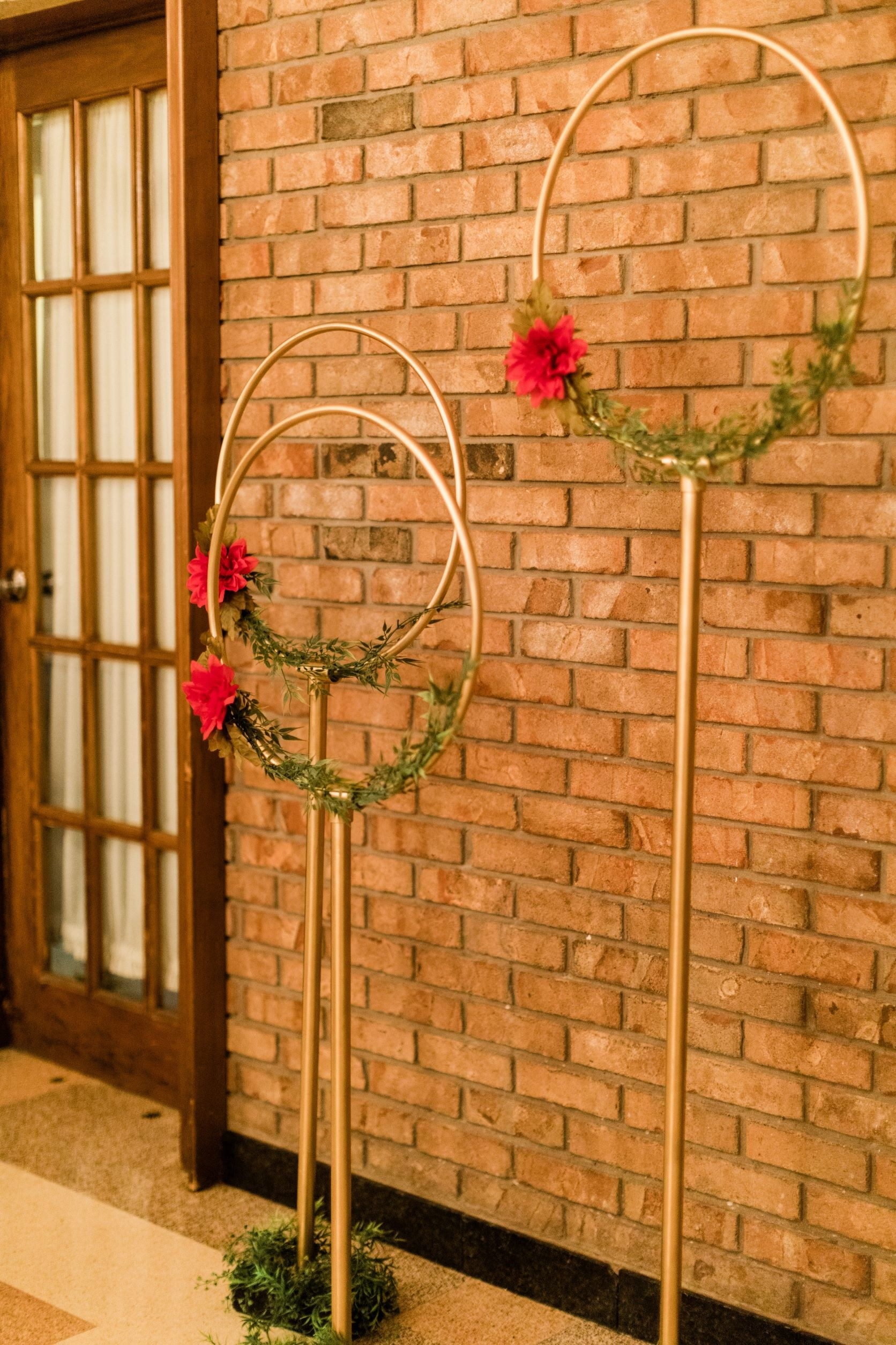 Three gold rods with hoops attached to the top. On the hoops are red flowers and greenery